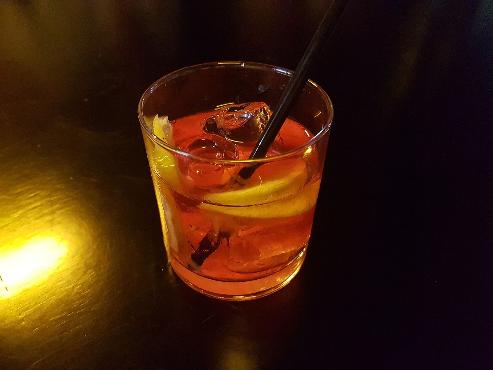 Un negroni con ghiaccio e scorza d'arancia su un bancone in penombra
