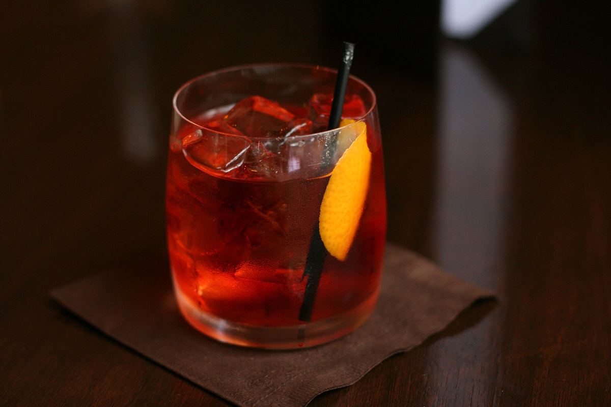Negroni con scorza d'arancia e cannuccia nera, appoggiato su un sottobicchiere